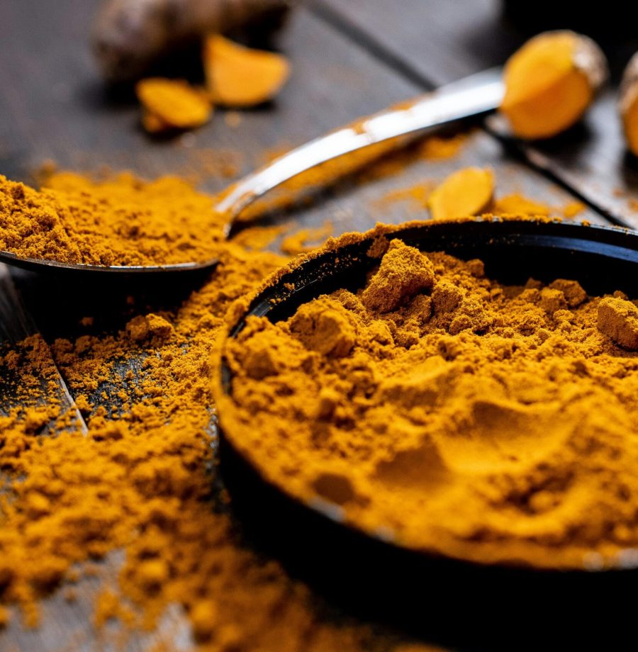 Close-up of vibrant turmeric powder with root on rustic wooden table, emphasizing texture and color.